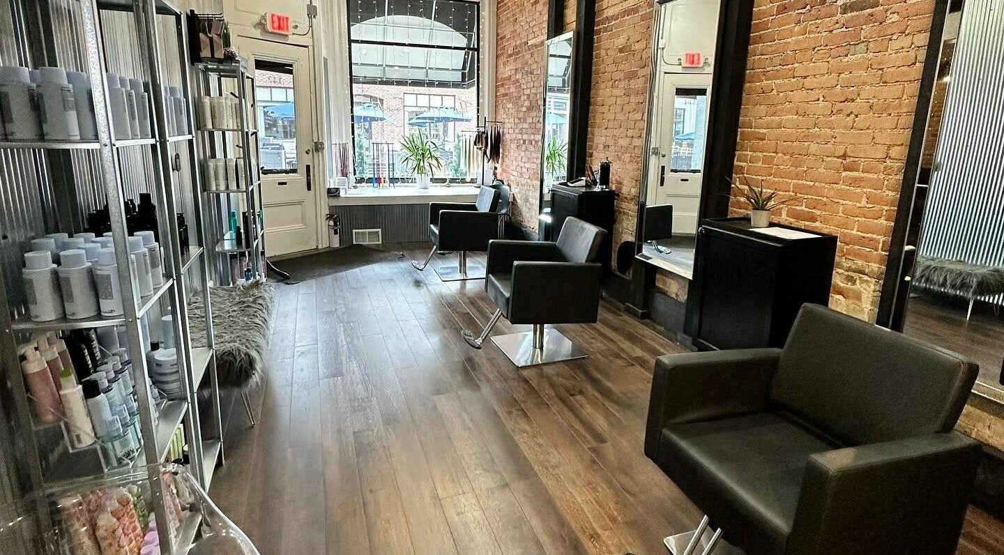 Modern salon interior at Jennifer at The Hair Foundation in Northville, Michigan, US with chic black chairs and product shelves.
