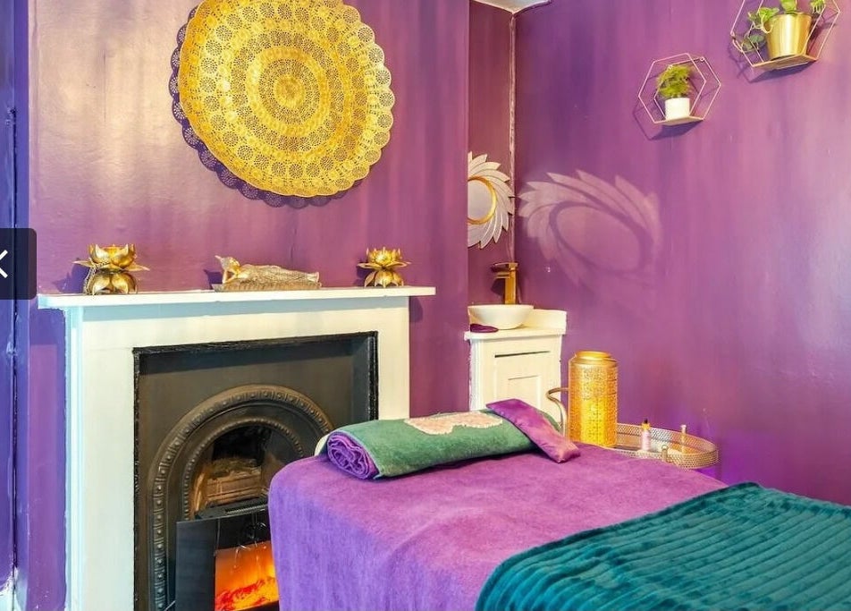 Relaxing massage room at Aura Organics Spa - Greenwich, London, England, GB, with purple decor and cozy fireplace.