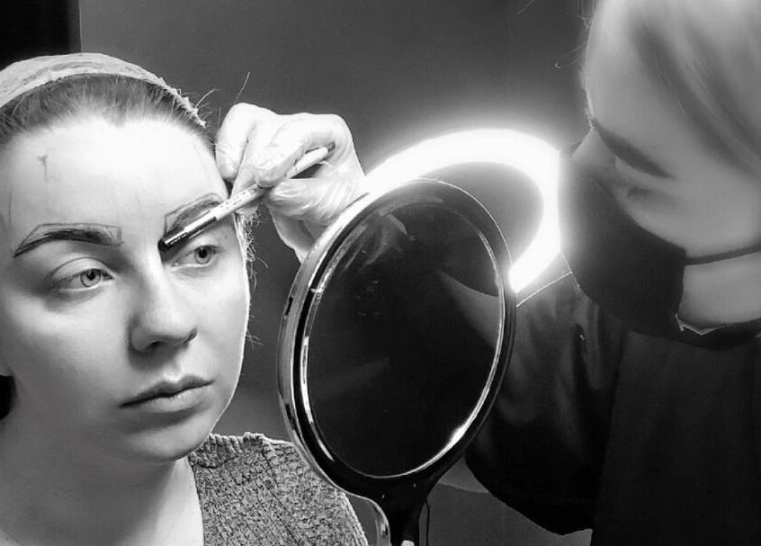 A beautician at ELR Cosmetics in Liverpool, England, GB, expertly shaping eyebrows with precision tools.
