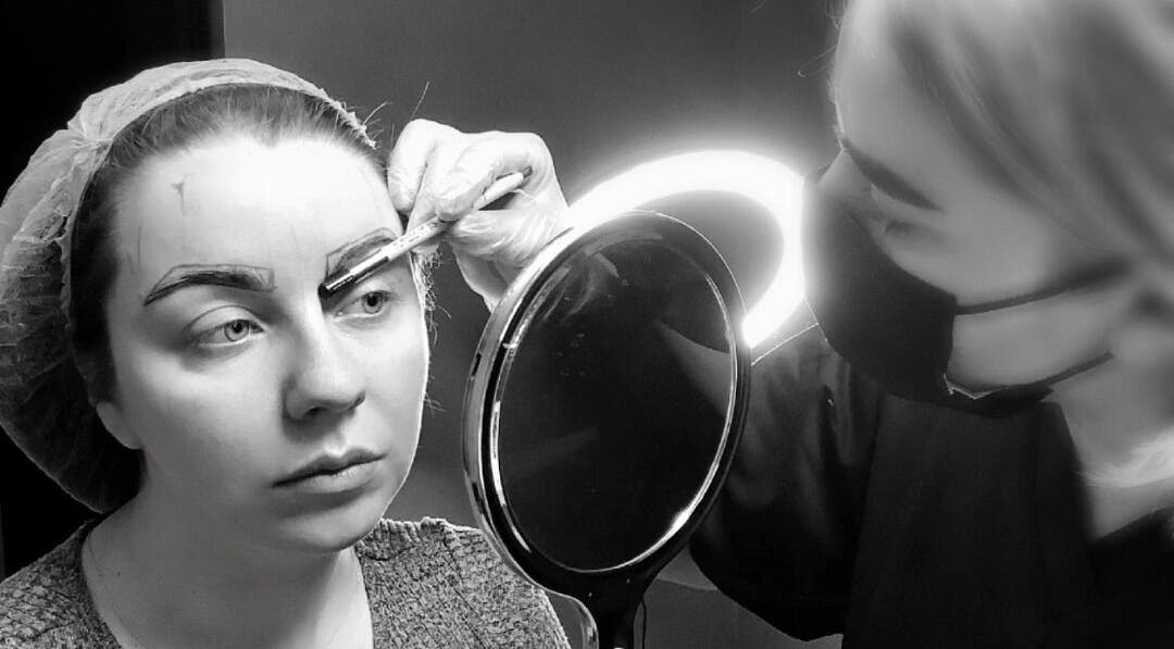 A beautician at ELR Cosmetics in Liverpool, England, GB, expertly shaping eyebrows with precision tools.