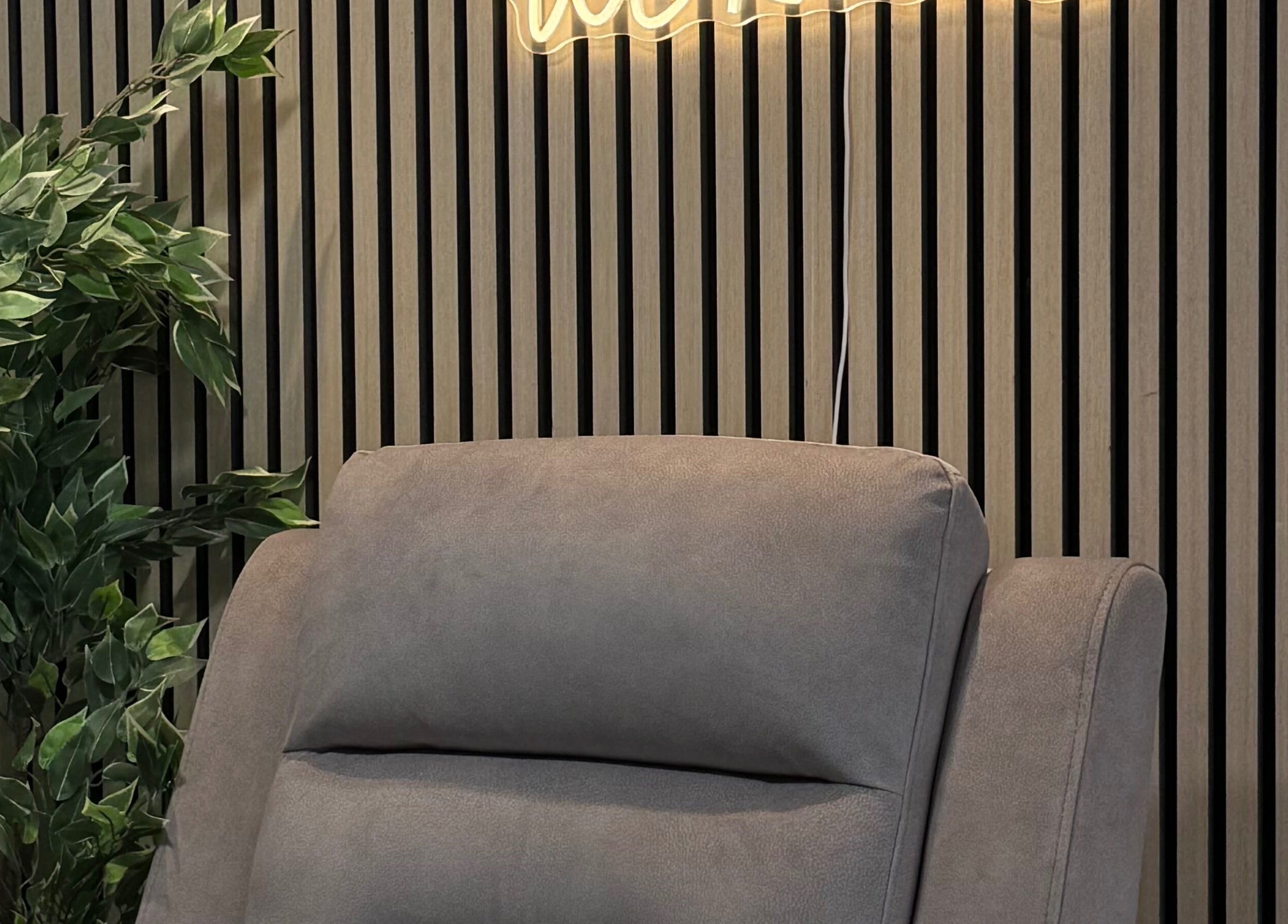 A cozy grey chair in Bloom Beauty, Tipperary, IE, with wooden paneling and greenery creating a tranquil ambiance.