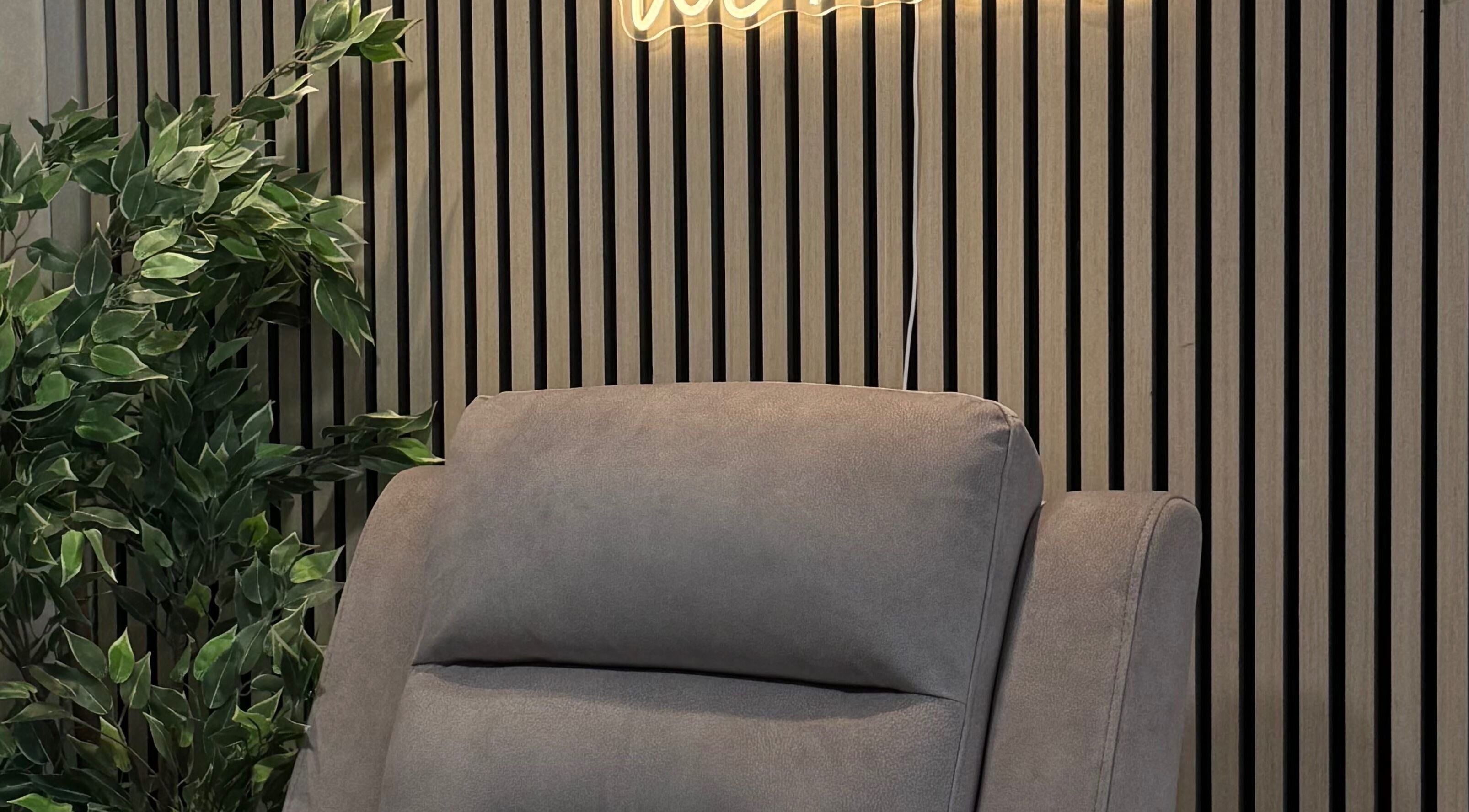 A cozy grey chair in Bloom Beauty, Tipperary, IE, with wooden paneling and greenery creating a tranquil ambiance.