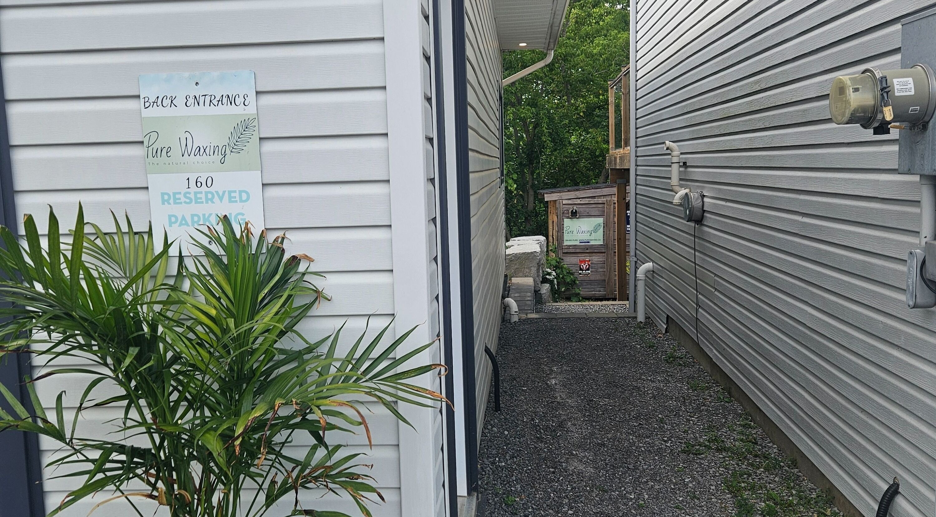 Back entrance to Pure Waxing in Quinte West, Ontario, CA, with lush green plants and a cozy path.