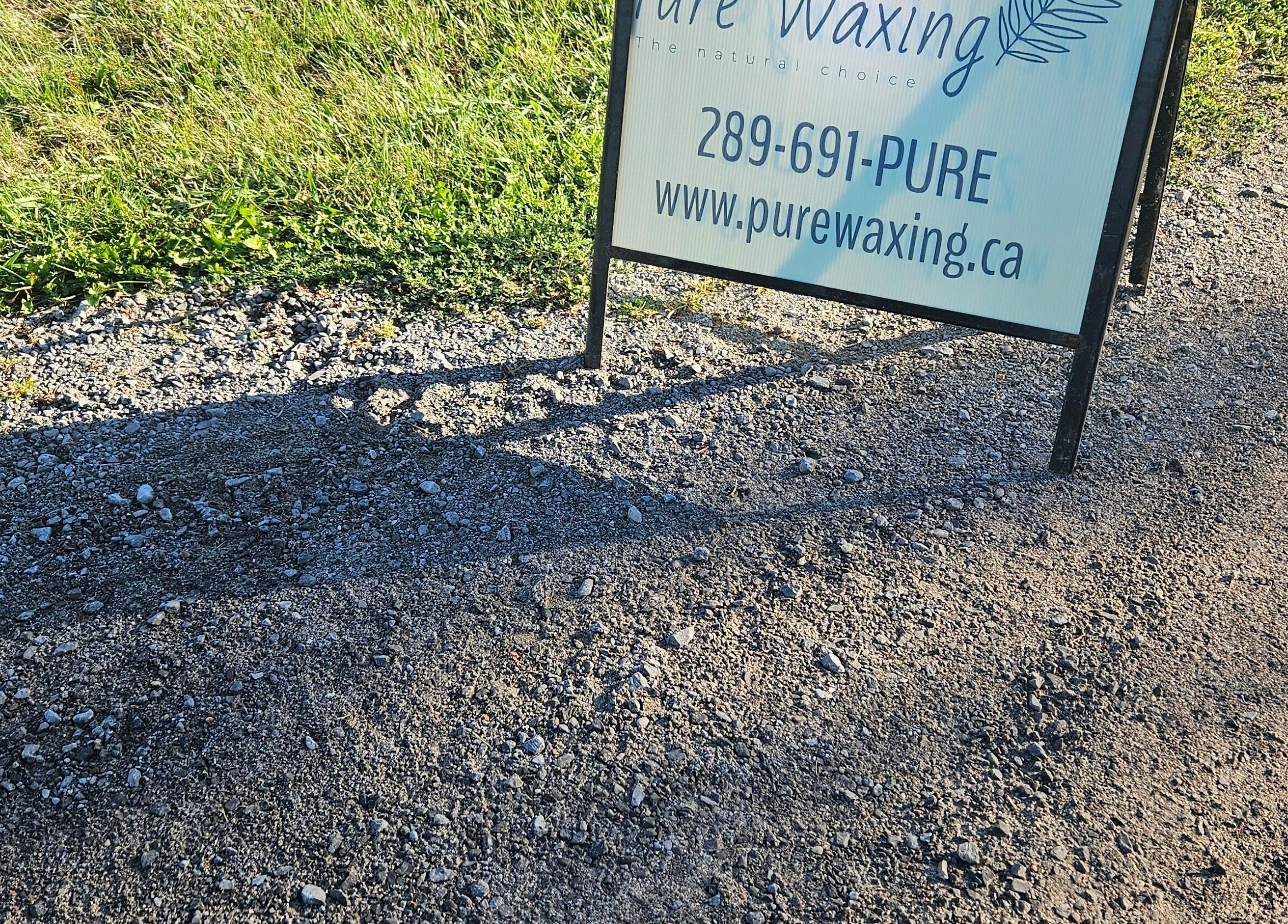 Outdoor sign for Pure Waxing at Quinte West, Ontario, CA graces a gravel pathway.
