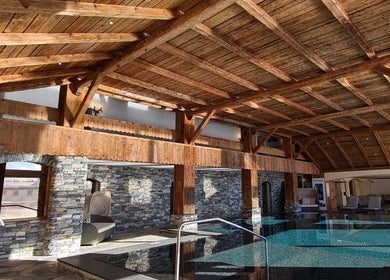 Piscine intérieure rustique à L'Alpage Spa, Crans-Montana, Valais, CH, avec plafond en bois et murs en pierre.