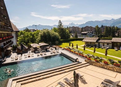 Vue sur la piscine extérieure luxueuse de L'Alpage Spa à Crans-Montana, Valais, CH, entourée de montagnes.