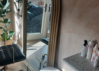 Modern salon chair and mirror at Carley Bayne Hair, Epsom, England, GB, with vibrant plant and hair products.