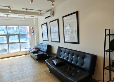 Interior modern The Cut Rumah Barber Paskal di Jawa Barat dengan sofa hitam dan pencahayaan alami.