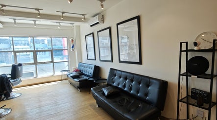 Interior modern The Cut Rumah Barber Paskal di Jawa Barat dengan sofa hitam dan pencahayaan alami.