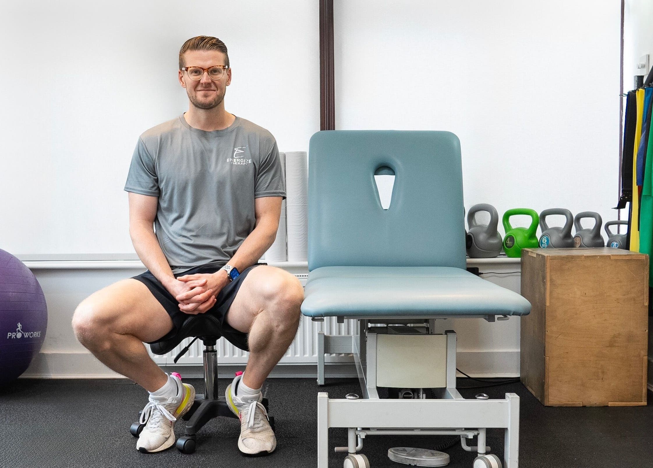 Therapist at Energize Therapy, Droitwich Spa, England, in a wellness room with fitness equipment.