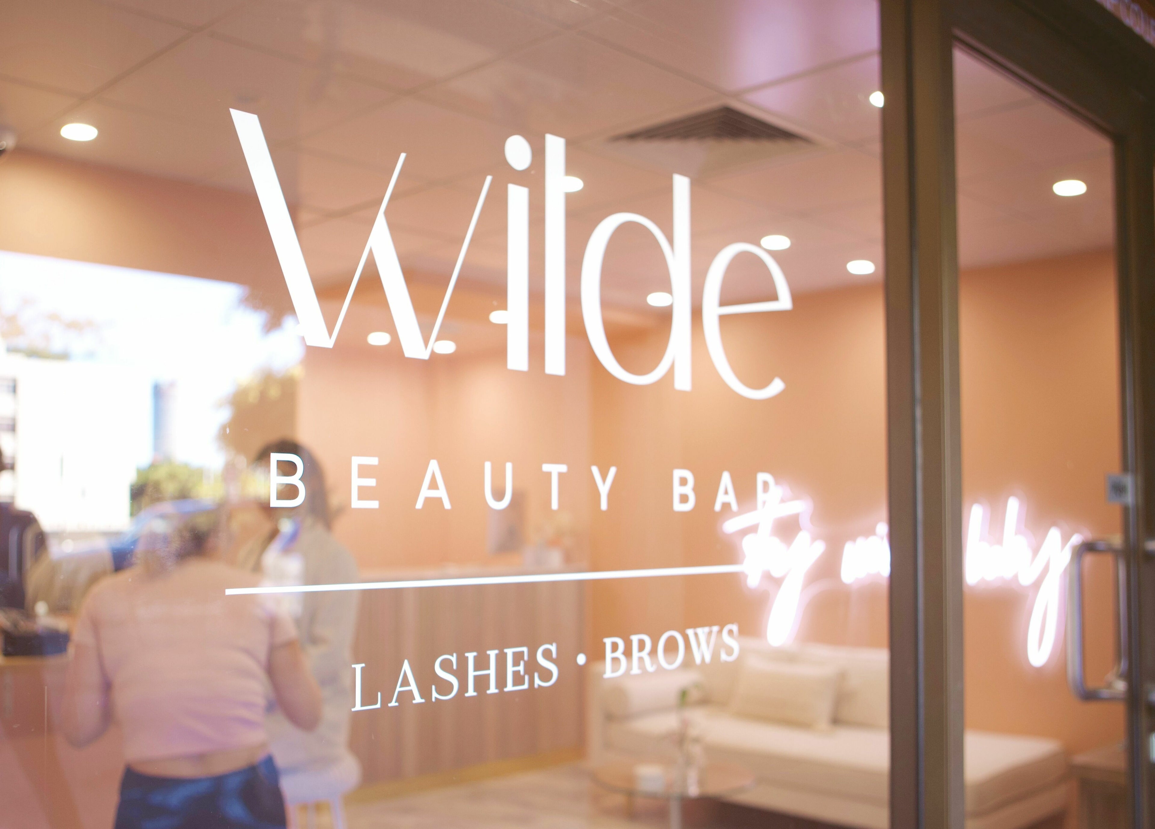Entrance of Wilde Beauty Bar in Bundall, Queensland, AU featuring stylish logo on glass doors.
