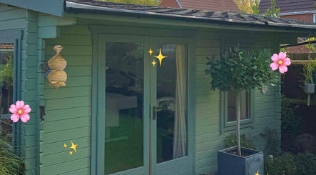 Peaceful garden retreat at Kora Beauty, Great Dunmow, England, GB, with green cabin and lush plants.