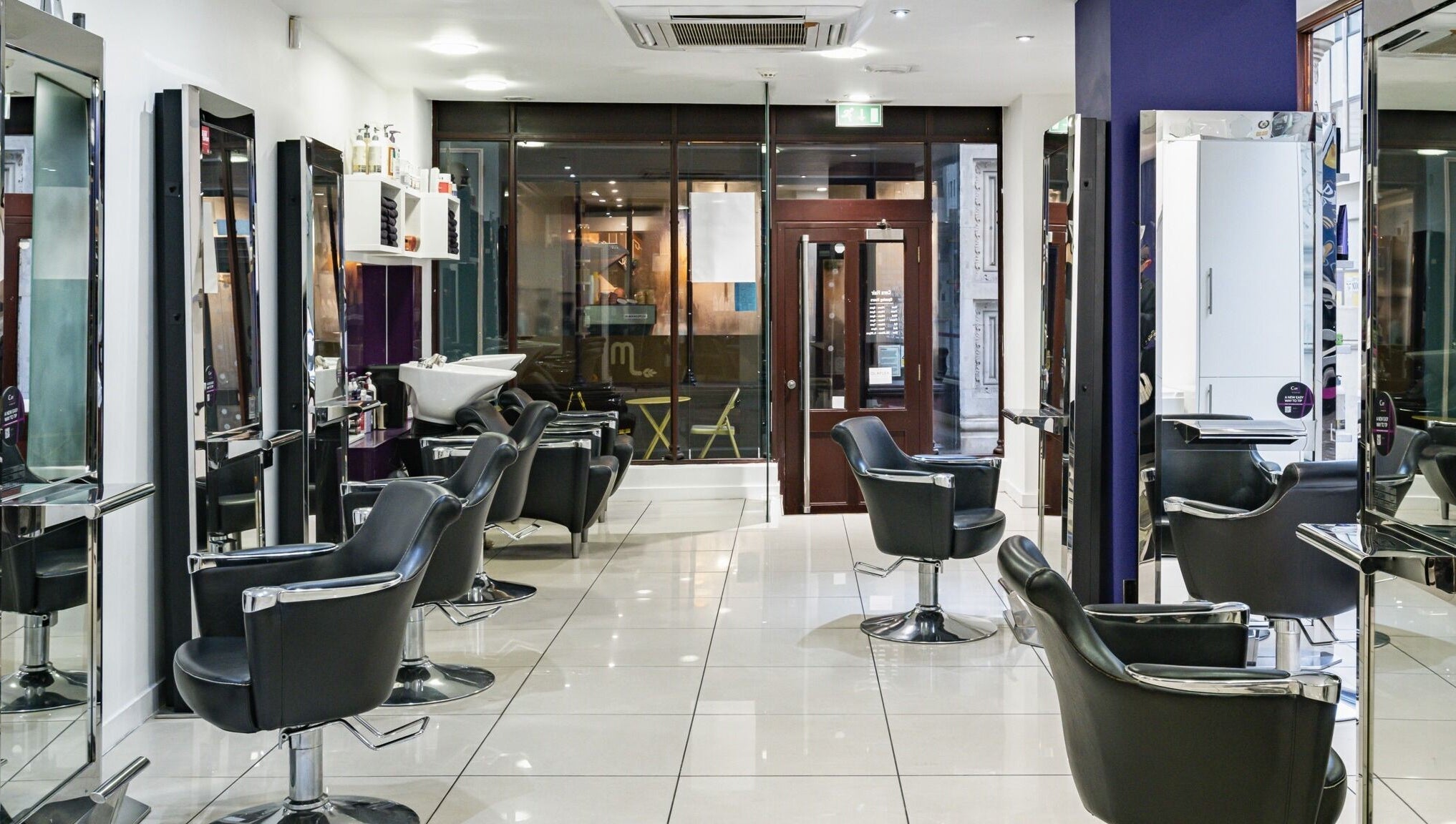 Modern interior of Cora Hair salon, Birmingham, England, GB, featuring sleek styling chairs and bright mirrors.