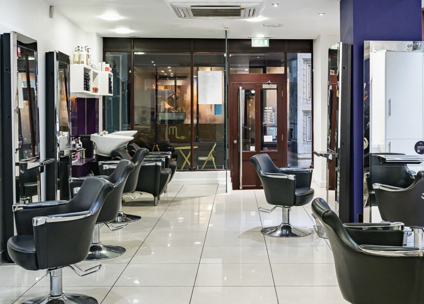 Modern interior of Cora Hair salon, Birmingham, England, GB, featuring sleek styling chairs and bright mirrors.
