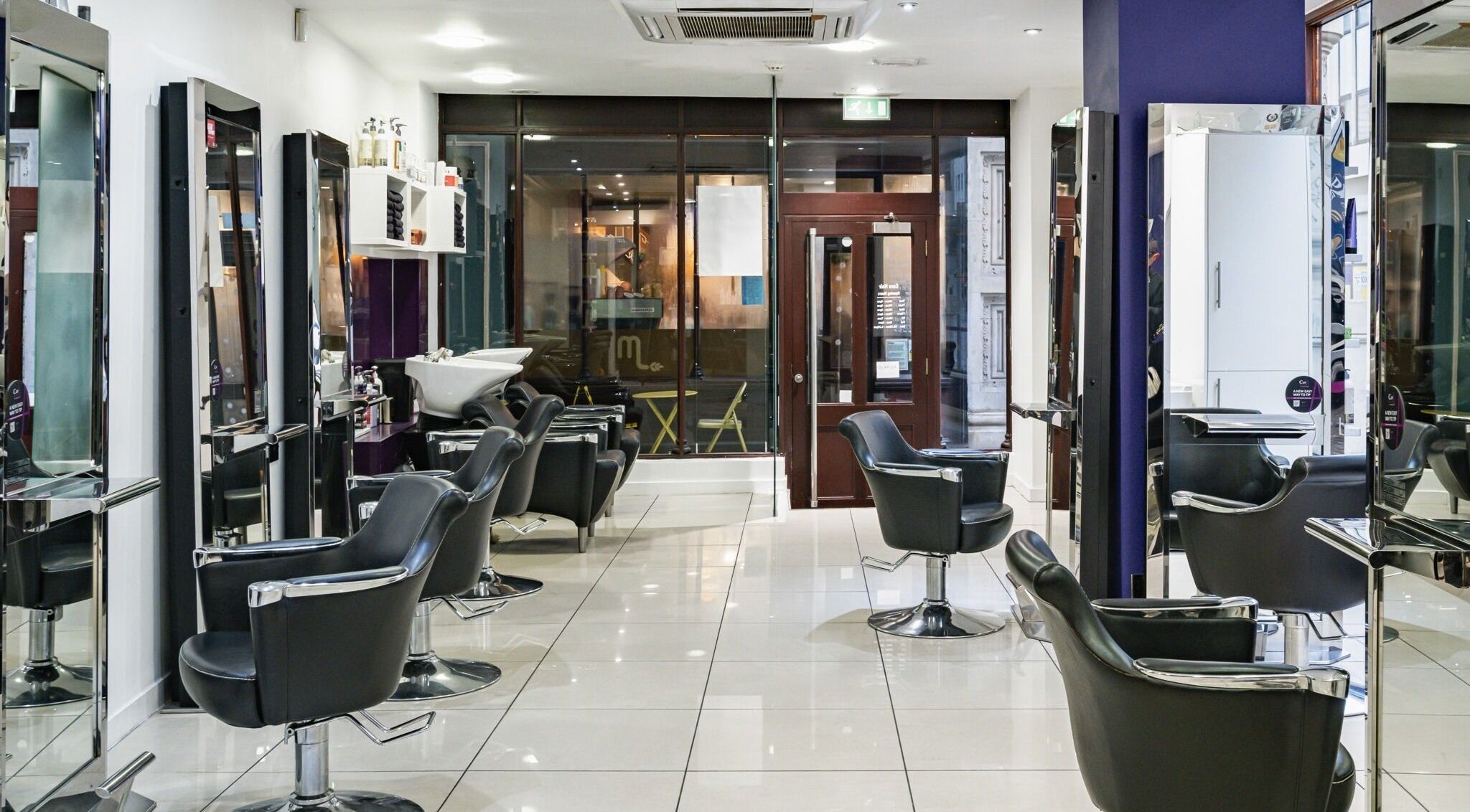 Modern interior of Cora Hair salon, Birmingham, England, GB, featuring sleek styling chairs and bright mirrors.