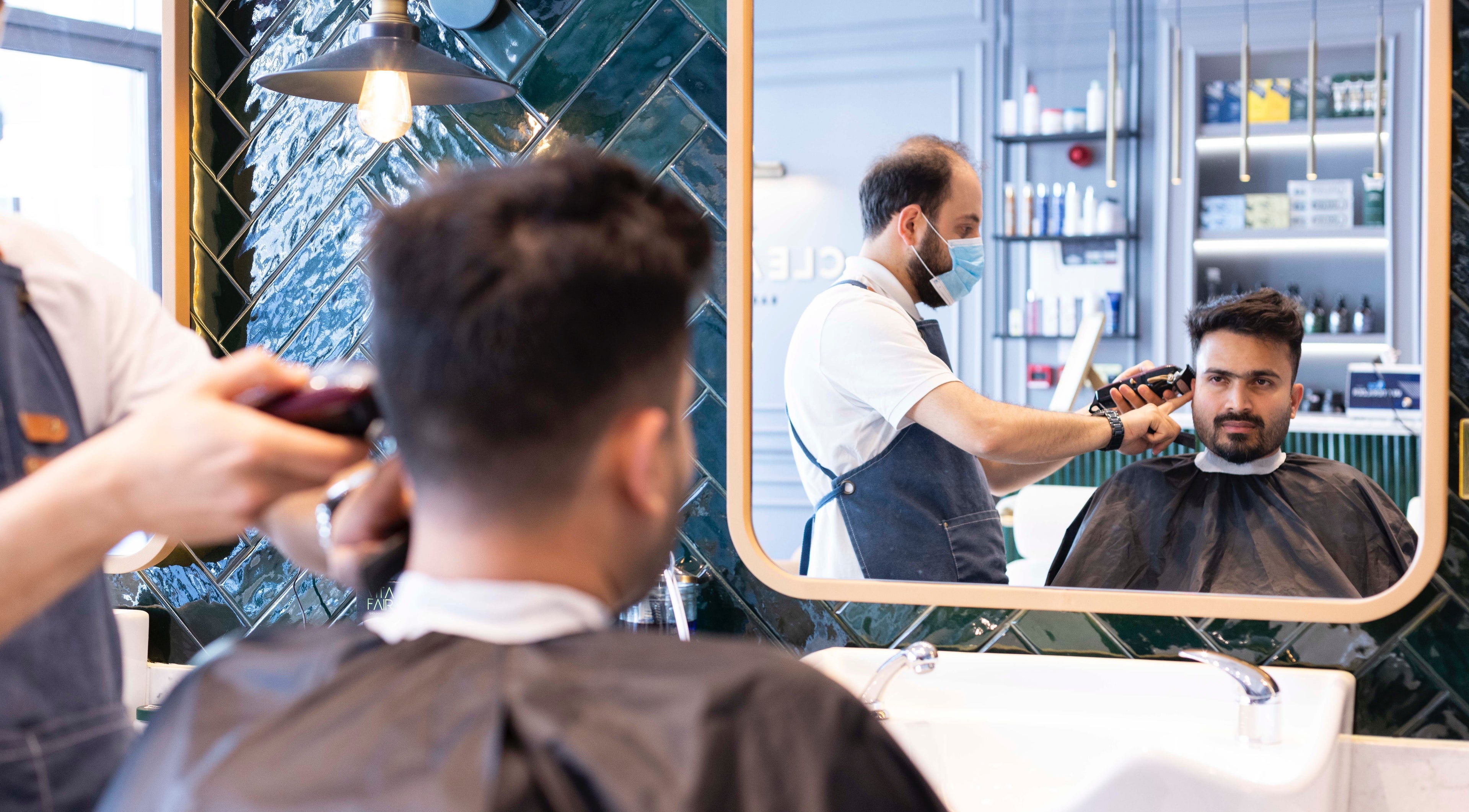 Barber at Clearcut Barbershop, Meshaf Crossings, Al Wukair, expertly trims a client's hair.