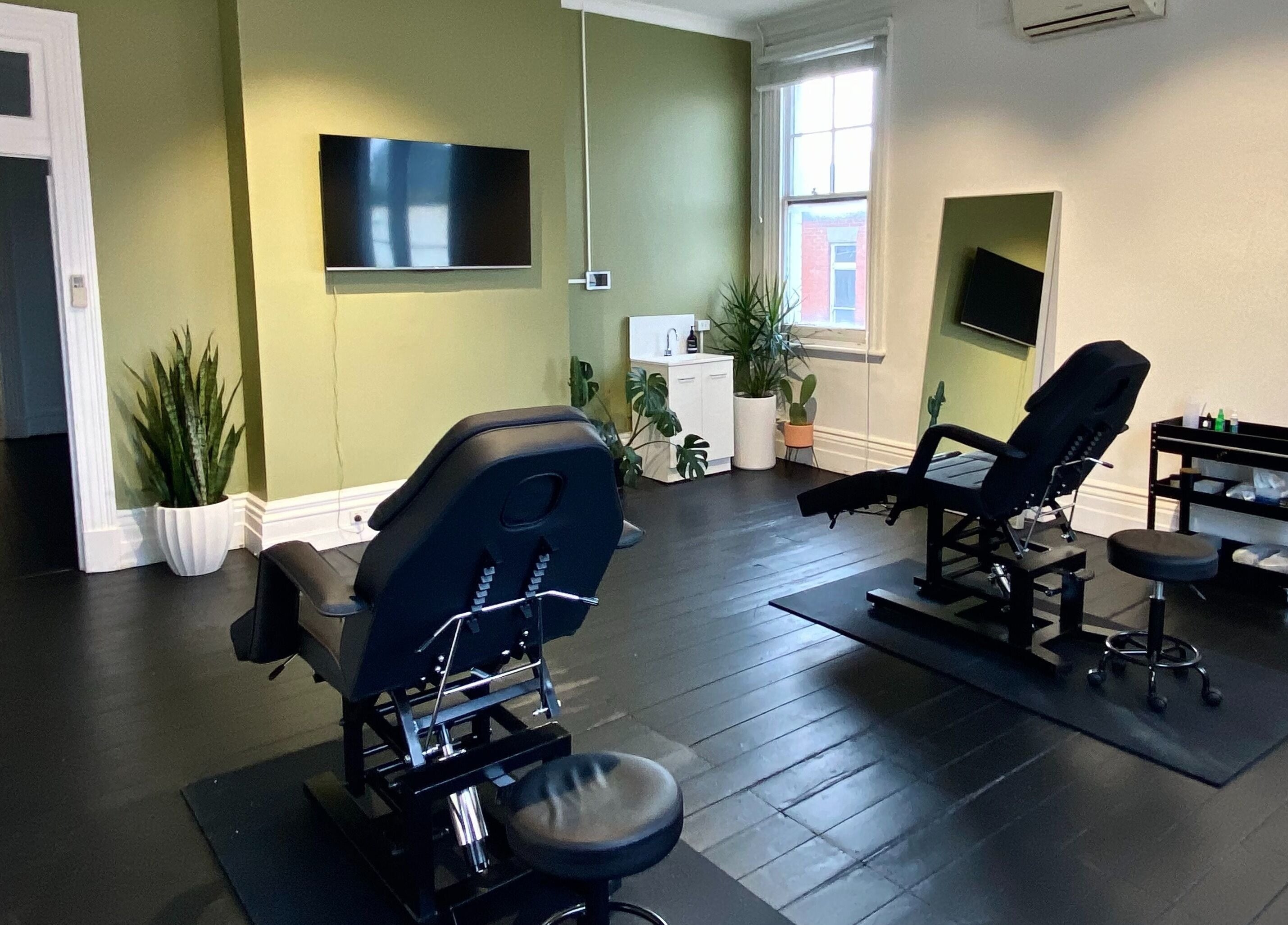 Modern treatment room at Inkd SMP in Melbourne, Victoria, AU with sleek chairs and soothing green walls.