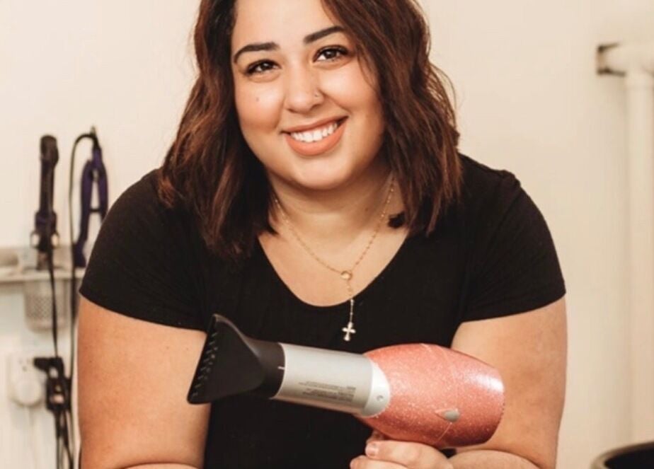Smiling hair stylist at Cabral Beauty in Bradford West Gwillimbury, Ontario, CA, holding a blow dryer.