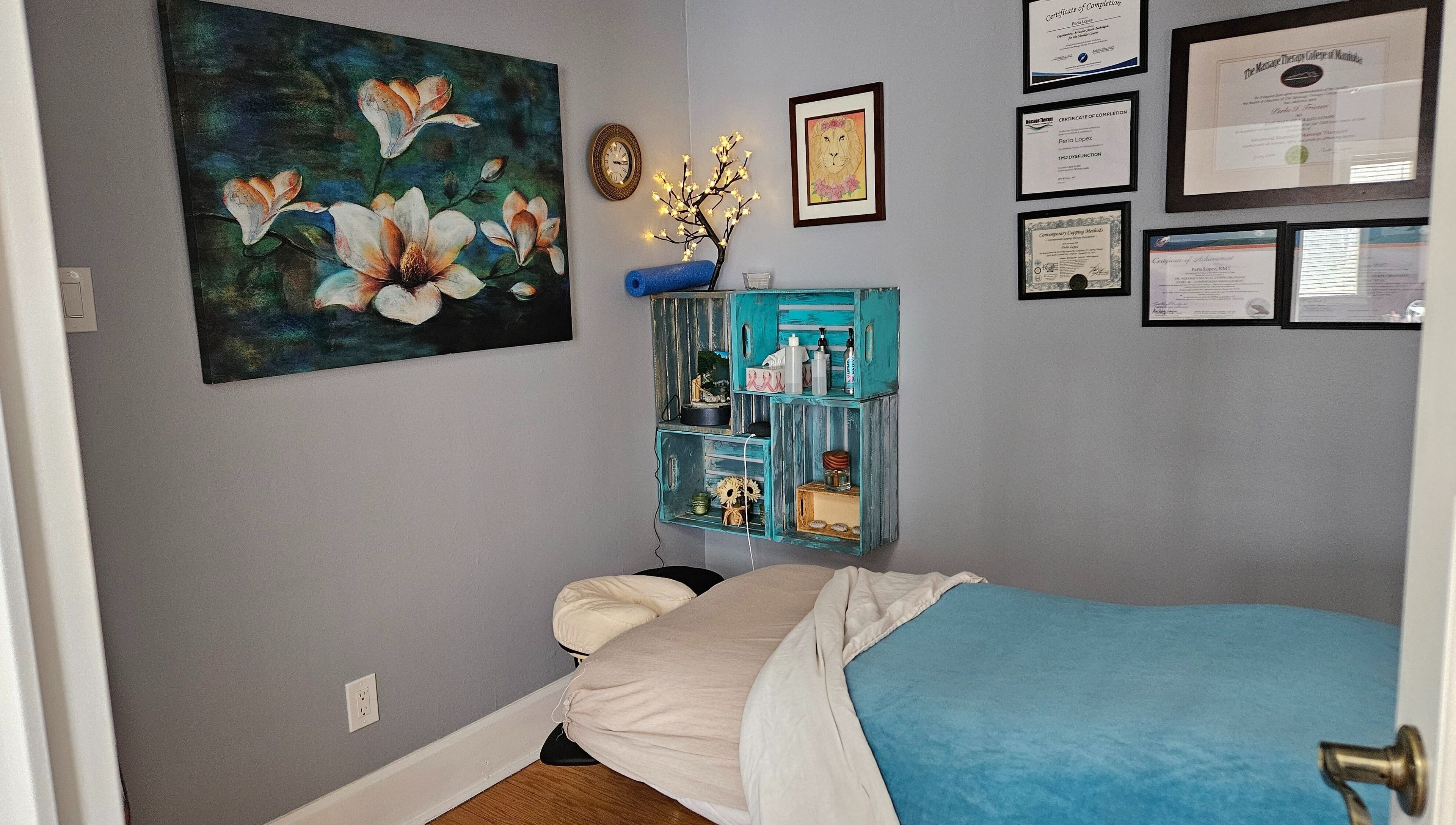 Cozy massage room at Natera Massage and Esthetics in Winnipeg, Manitoba, CA, adorned with certificates and floral decor.