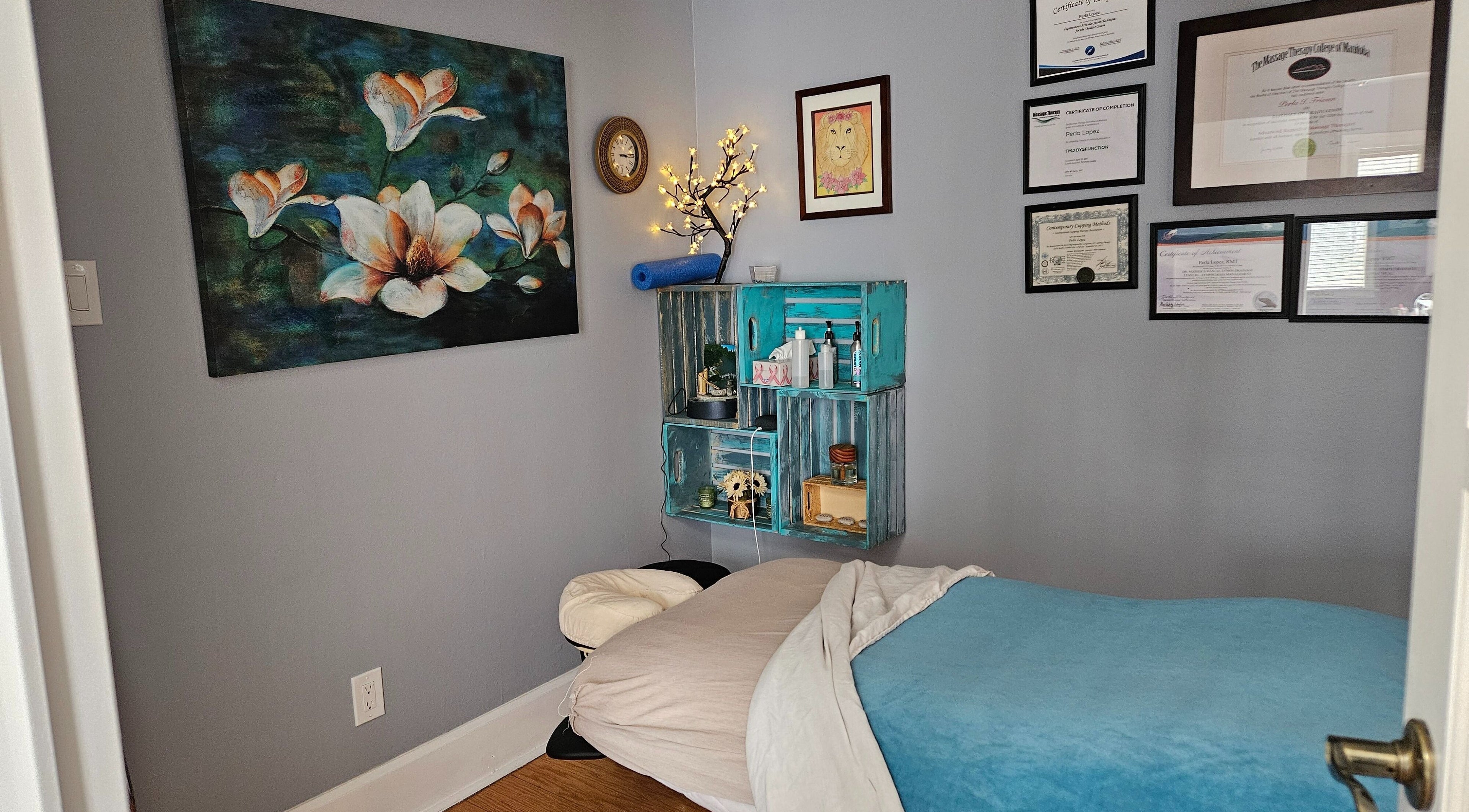 Cozy massage room at Natera Massage and Esthetics in Winnipeg, Manitoba, CA, adorned with certificates and floral decor.