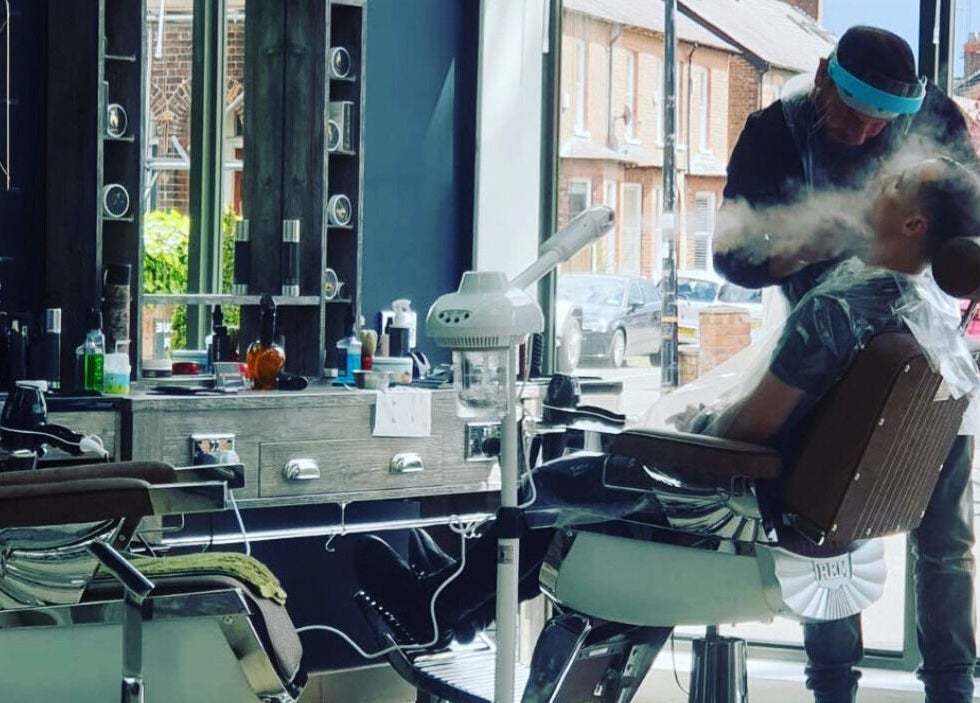 Professional barber styling client at Le Vogue Barber, Bowdon, England, GB, in a modern, sunlit setting.