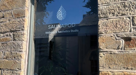 Saunapod's glass window reflects wellness studio in Falmouth, England, GB with stone wall background.