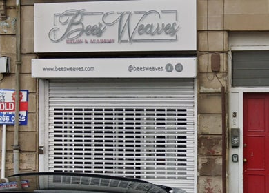 Front view of bees. salon in Paisley, Scotland, GB with a closed shutter and a sign above.
