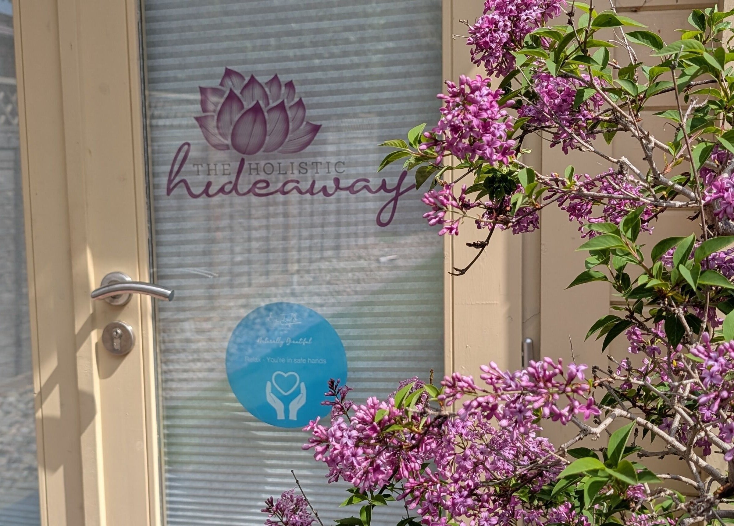 Entrance of The Holistic Hideaway in Saint Neots, England with purple flowers and logo visible.