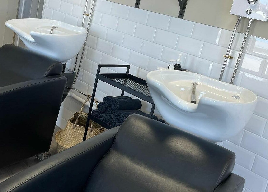 Modern wash stations at Stef Hayes Hair in Bude, England, GB, featuring sleek black chairs and white basins.