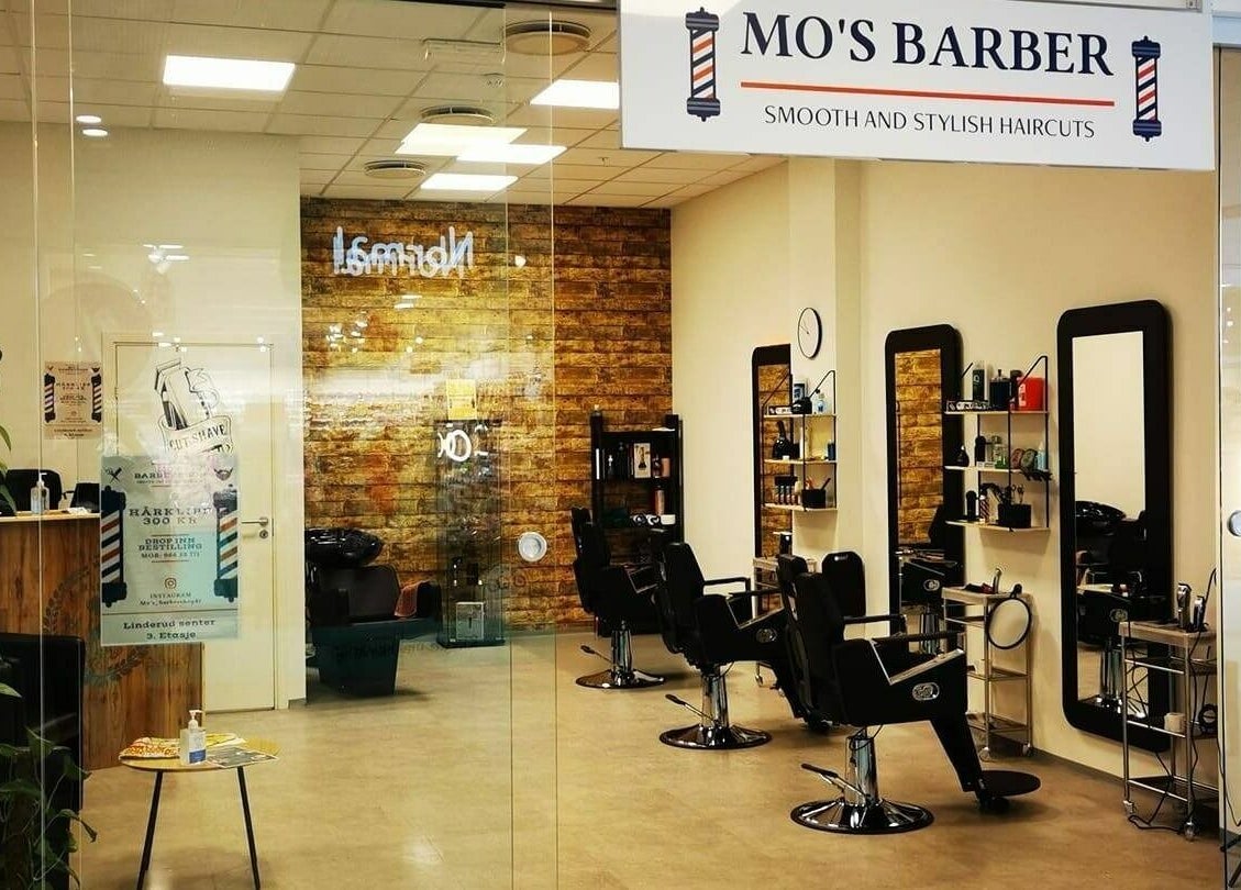 Stilig interiør på Mo's Barber i Oslo, Oslo, NO med sorte stoler og speil langs veggen.