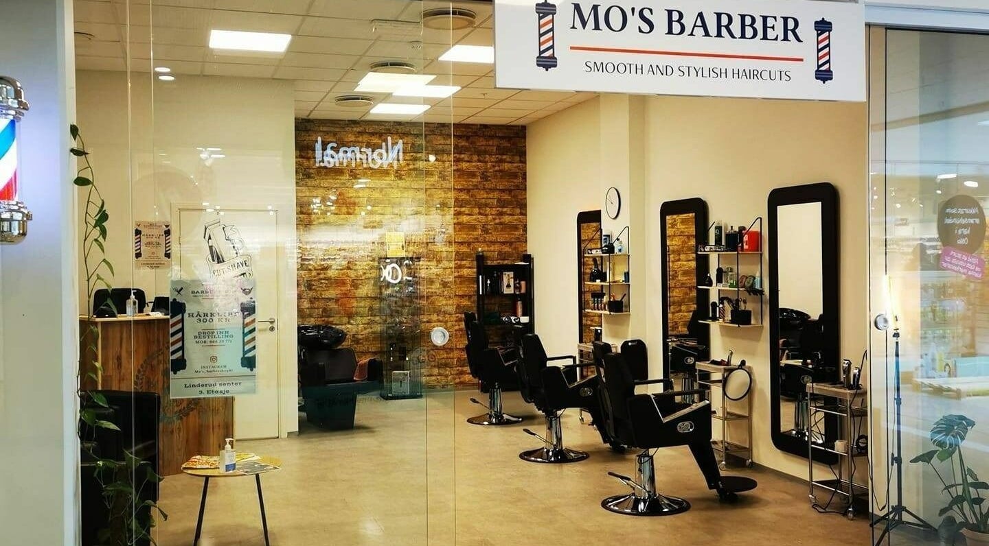 Stilig interiør på Mo's Barber i Oslo, Oslo, NO med sorte stoler og speil langs veggen.