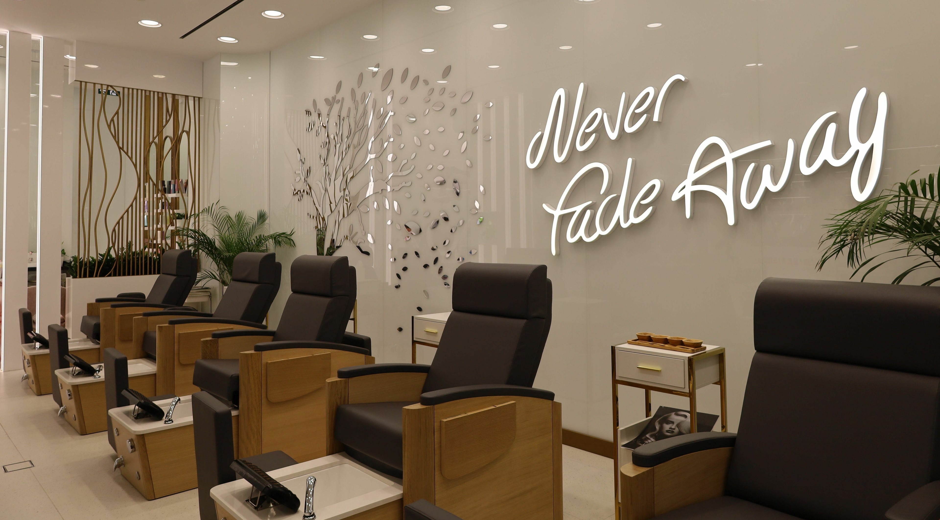 Chic pedicure chairs at WOW Beauty Salon Reem Mall, Abu Dhabi, AE, with modern decor and 'Never Fade Away' sign.