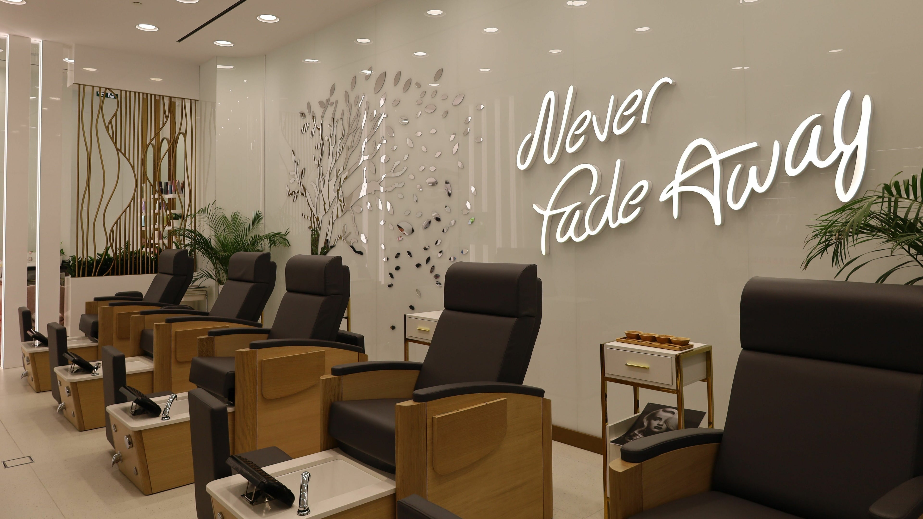 Chic pedicure chairs at WOW Beauty Salon Reem Mall, Abu Dhabi, AE, with modern decor and 'Never Fade Away' sign.