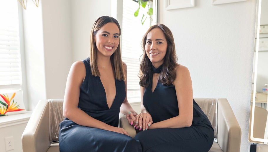 Two women in black outfits seated in Team Lilian Sanchez salon, Katy, Texas, US, smiling warmly.