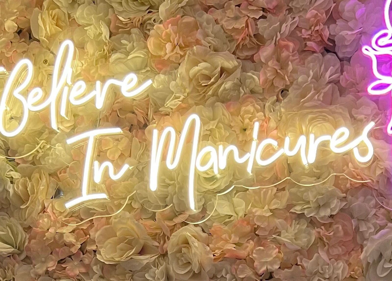 Neon sign at Rose Nails in Barking, England with floral background saying 'I Believe In Manicures'.