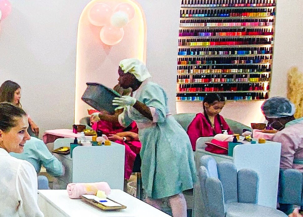 Clientes recebendo manicures no Glow, Maputo, Maputo, MZ, com parede de esmaltes e decorações balão.
