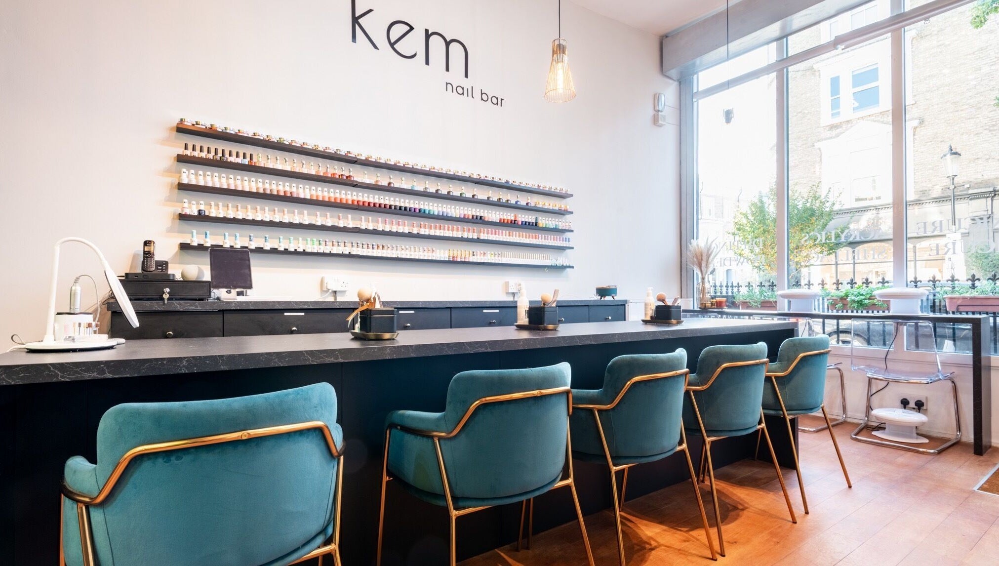 Modern interior of Kem Nail Bar in London, England, GB with plush teal chairs and nail polish display.