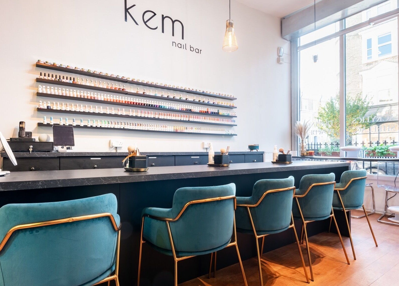 Modern interior of Kem Nail Bar in London, England, GB with plush teal chairs and nail polish display.