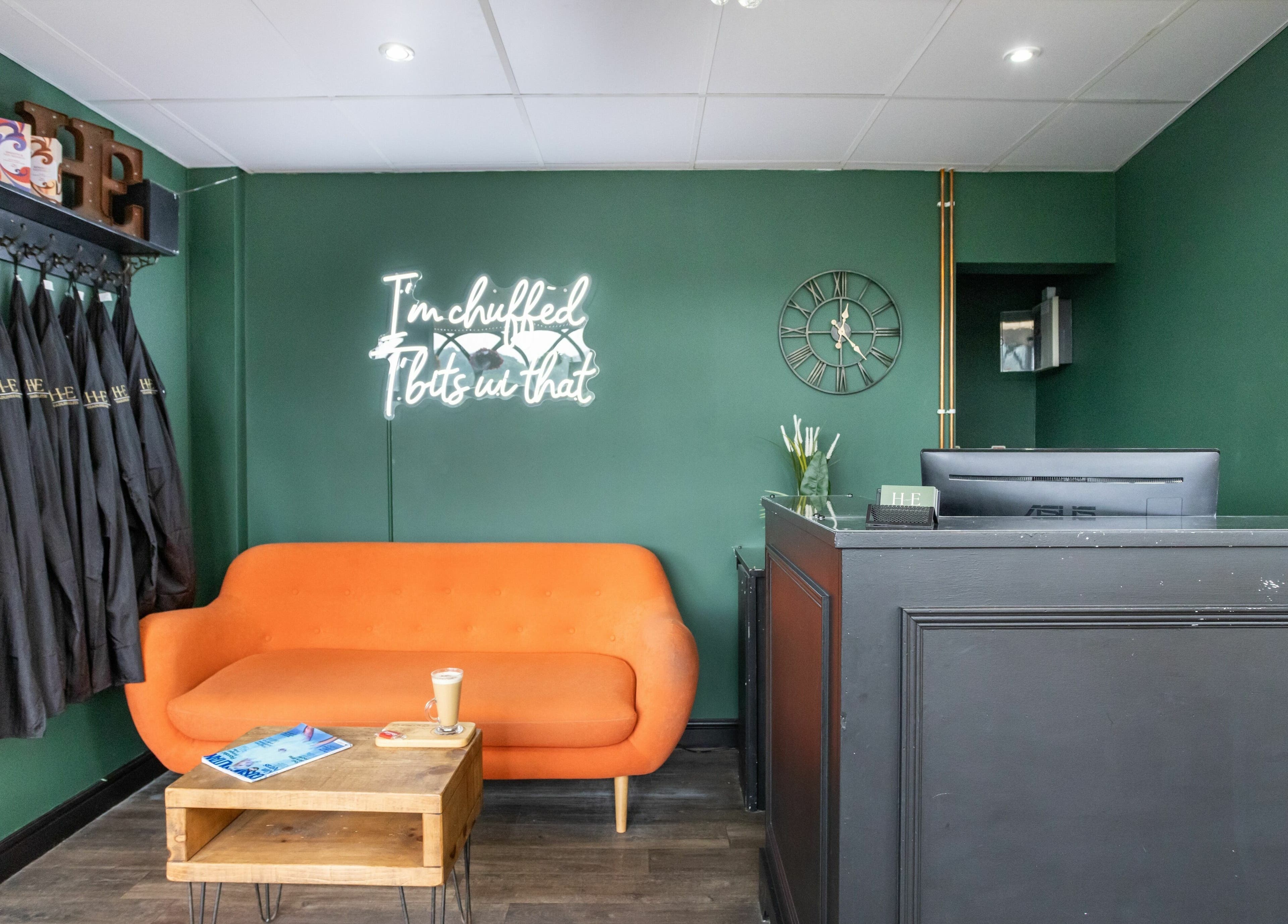 Cozy lounge with orange sofa at Headlines Elite, Sheffield, England, GB. Features robes, neon sign, and reception desk.