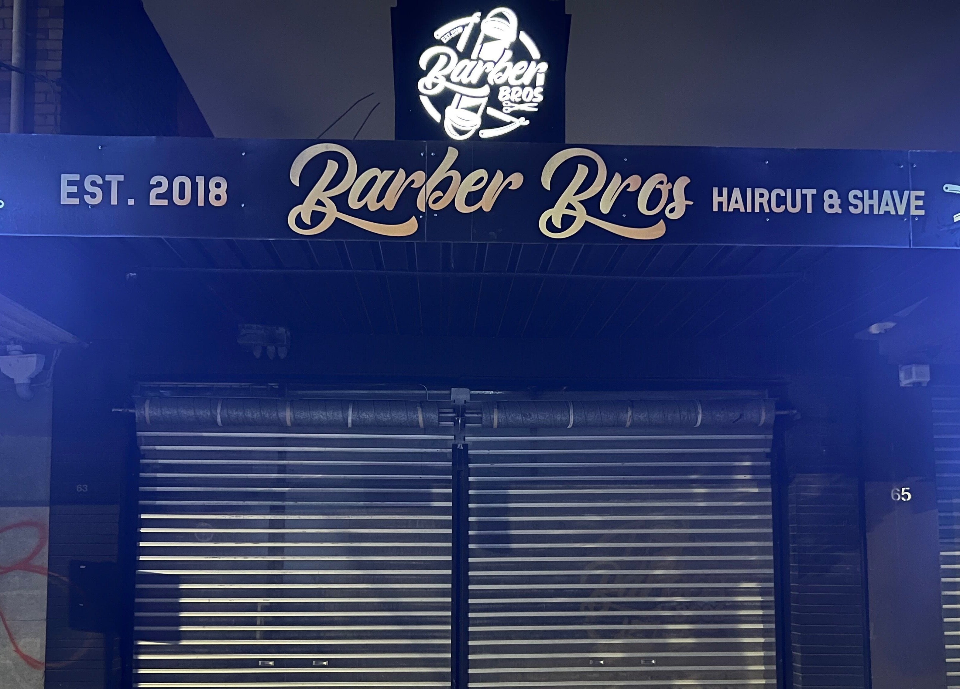 Illuminated Barber Bros sign in Melbourne, Victoria, AU showcasing haircuts and shaves.