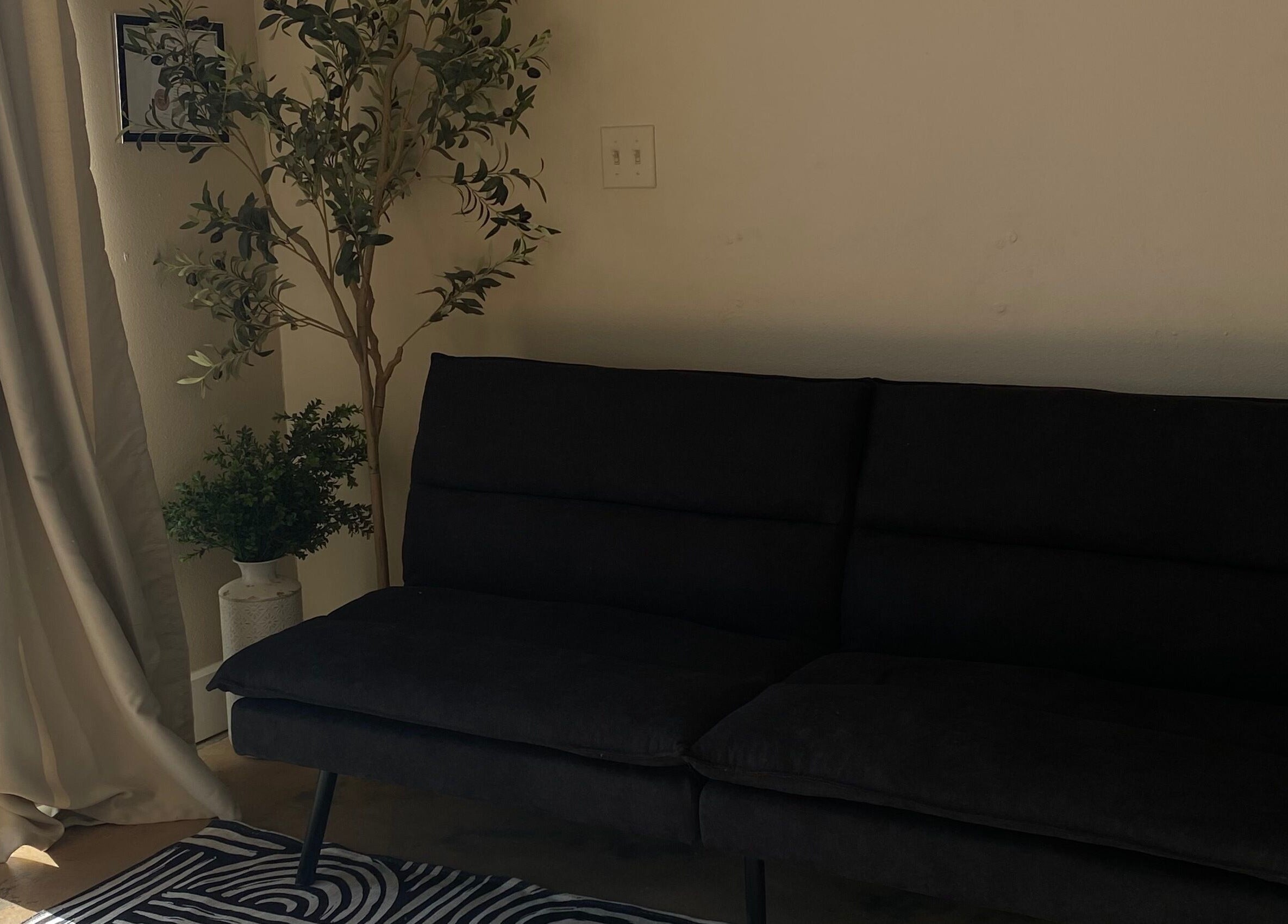 Elegant seating area at Sculpted by Perla, Fort Mohave, Arizona, US featuring dark sofa and greenery.