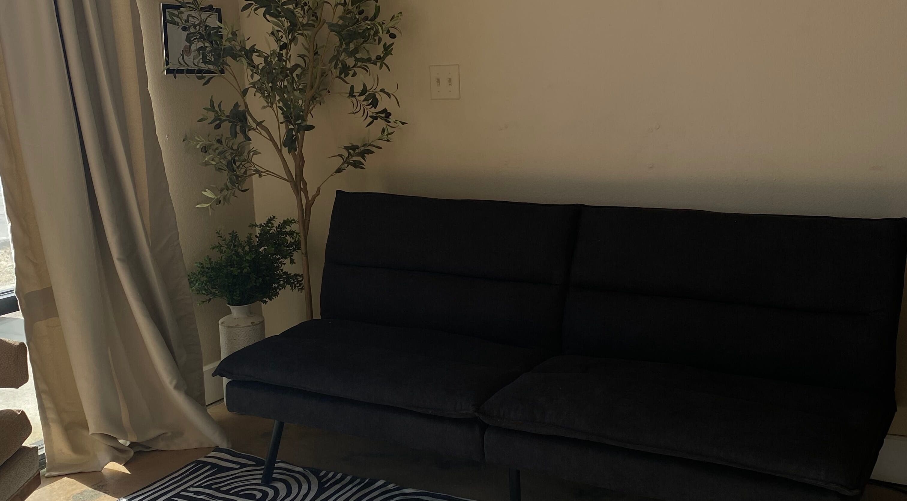 Elegant seating area at Sculpted by Perla, Fort Mohave, Arizona, US featuring dark sofa and greenery.