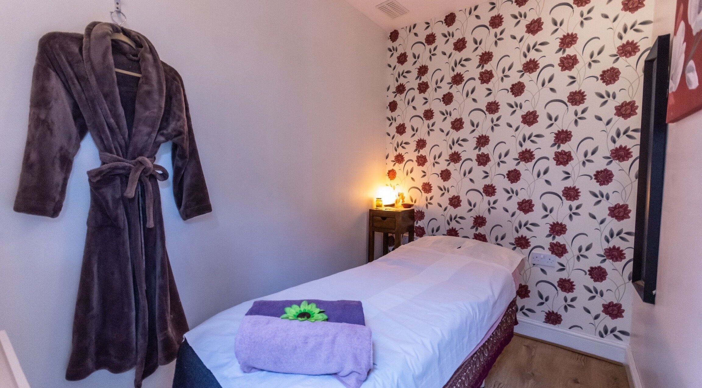 Tranquil massage room at Dee Therapy & Salon, Harrow, England, GB with cozy robe and floral decor.