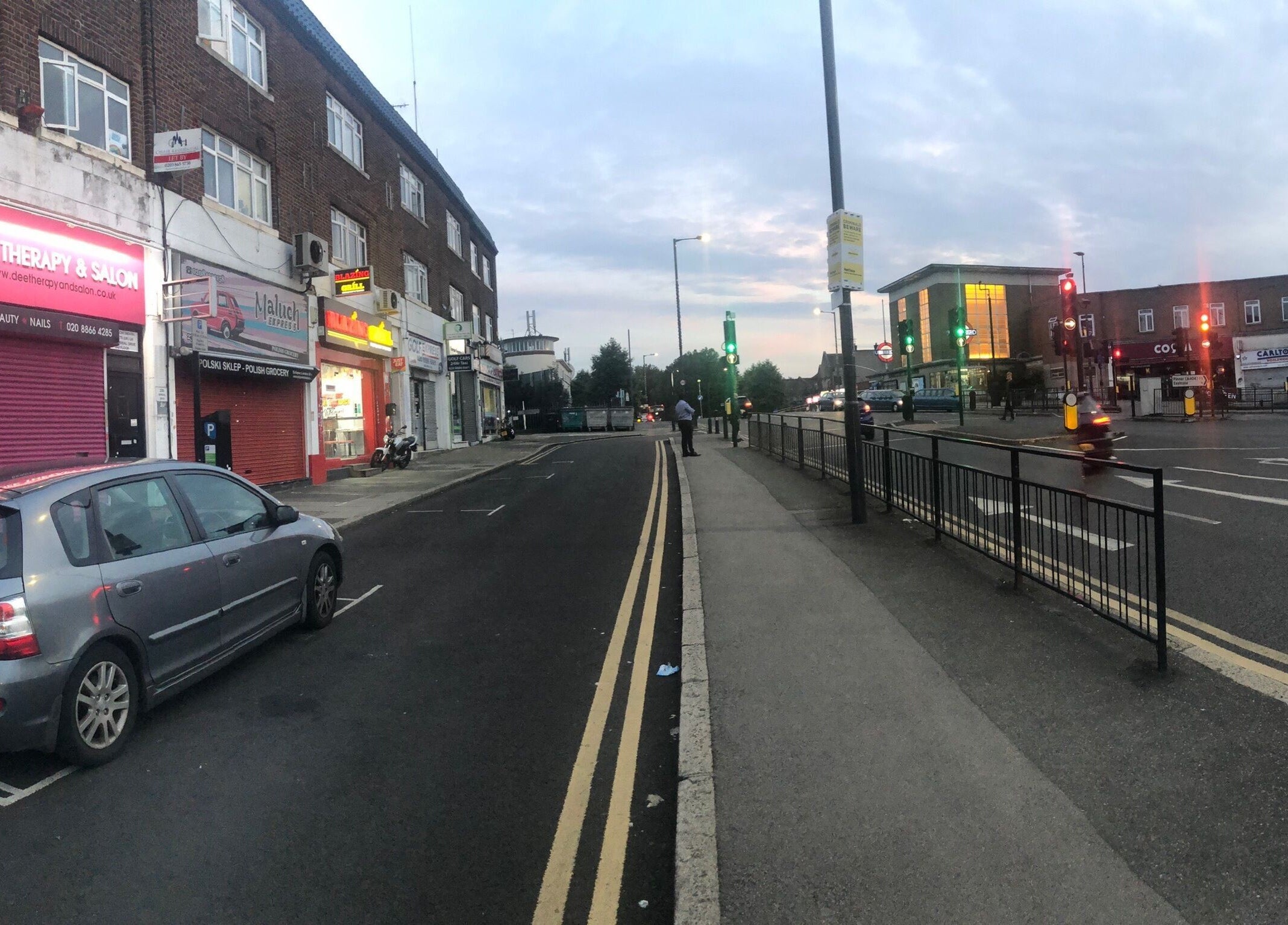 Street view of Dee Therapy & Salon, Harrow, England, GB at dusk with streetlights and nearby shops.