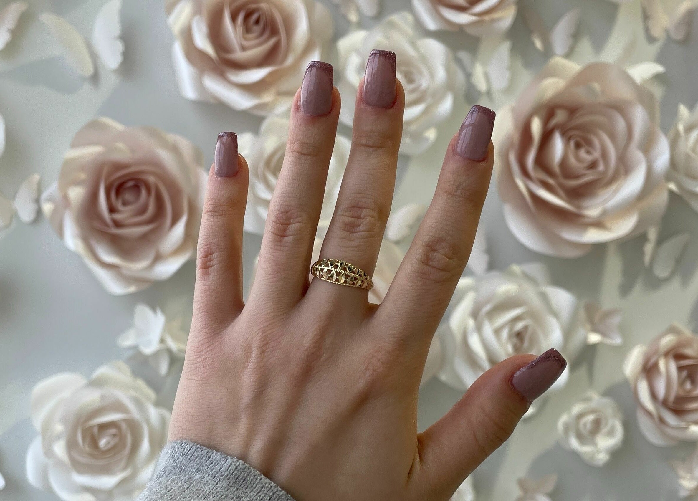Hand with mauve manicure and gold ring at Nails a More Woodbridge, Vaughan, Ontario, CA, against rose backdrop.