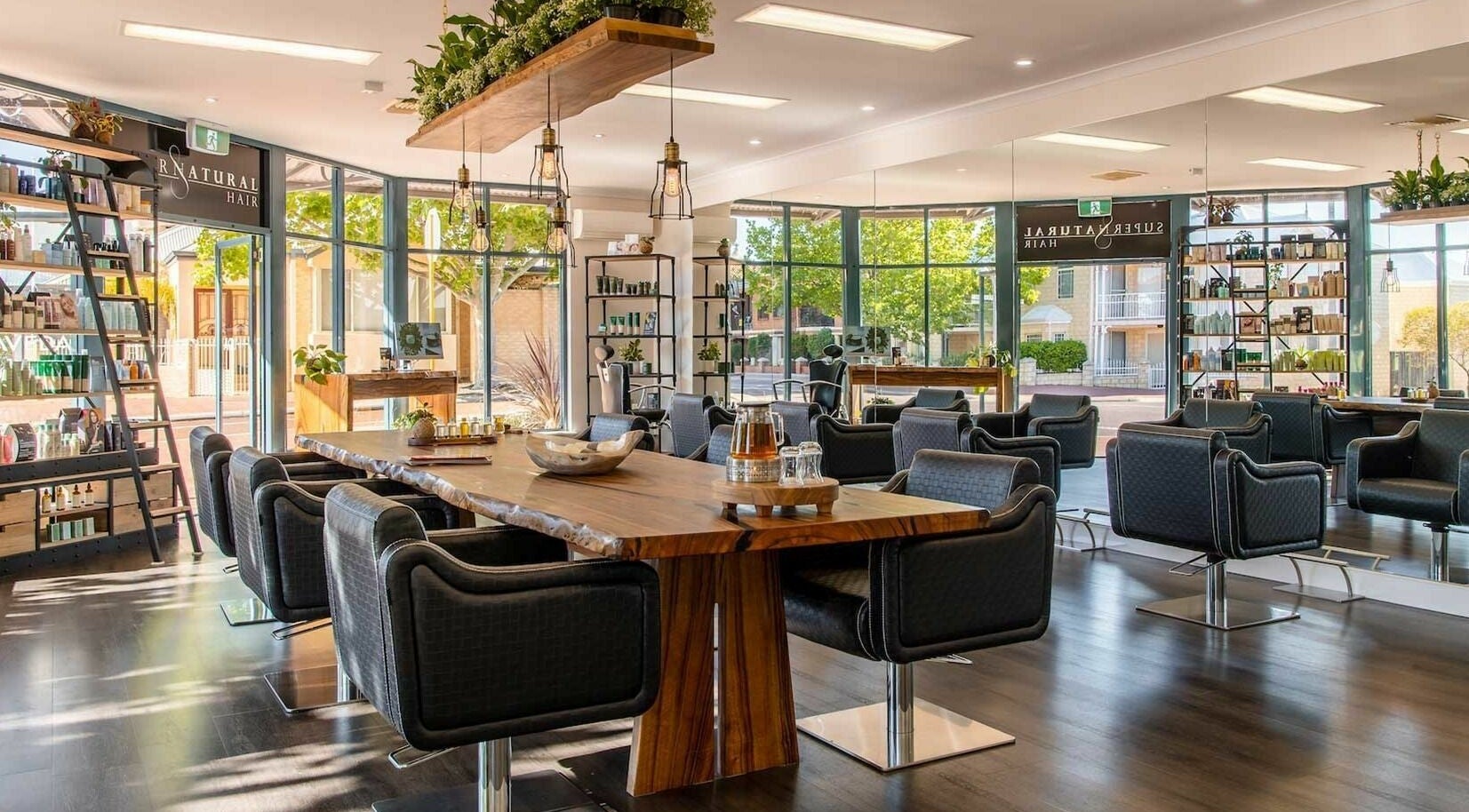 Interior of Supernatural Hair in Joondalup, Western Australia, AU, showcasing modern styling chairs and wooden table.