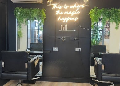 Stylish salon chairs and mirrors at THE GLOSS, Lowestoft, England, GB with neon sign and greenery.