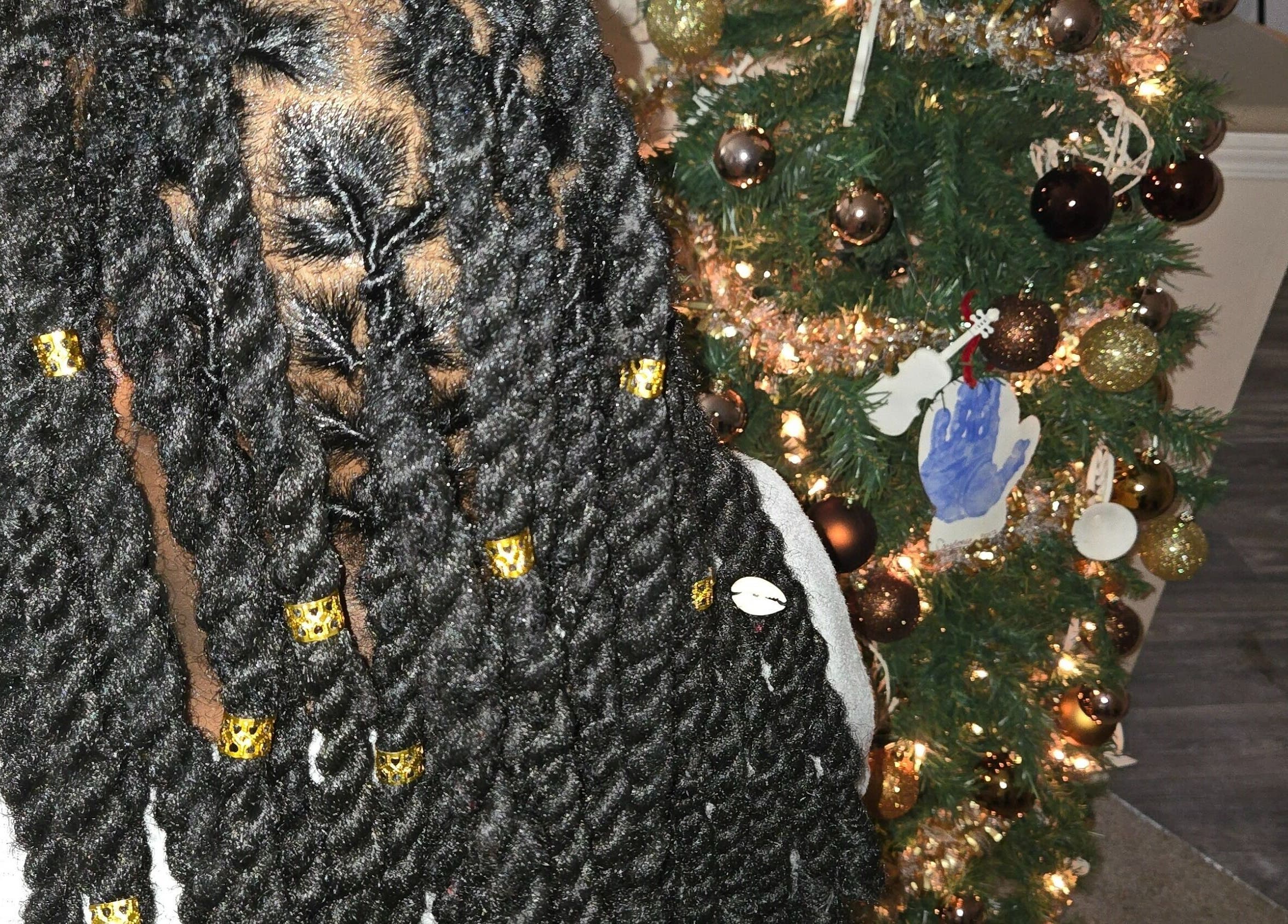 Elegant braids adorned with gold cuffs at Naturally Loc'd by Ci, Charlotte, North Carolina, US, near a decorated tree.
