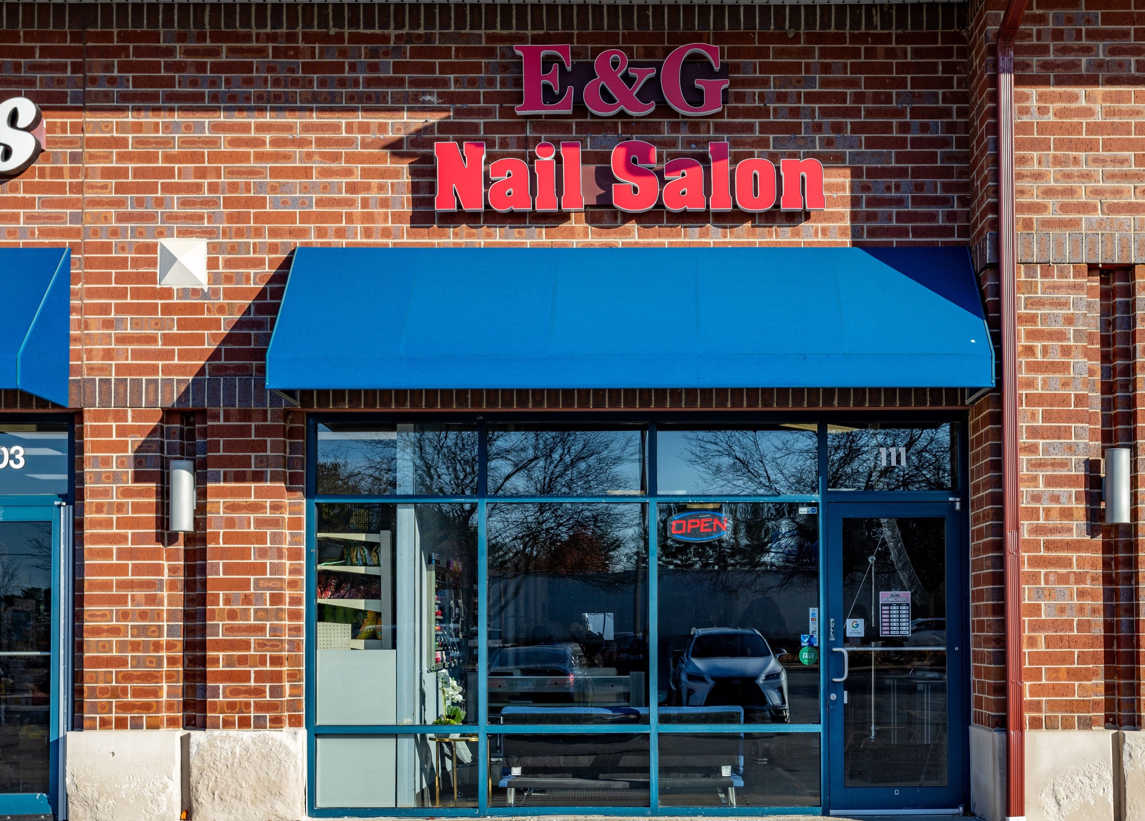 Front view of EG Nails & Spa in Naperville, Illinois, US with a brick exterior and blue awnings.