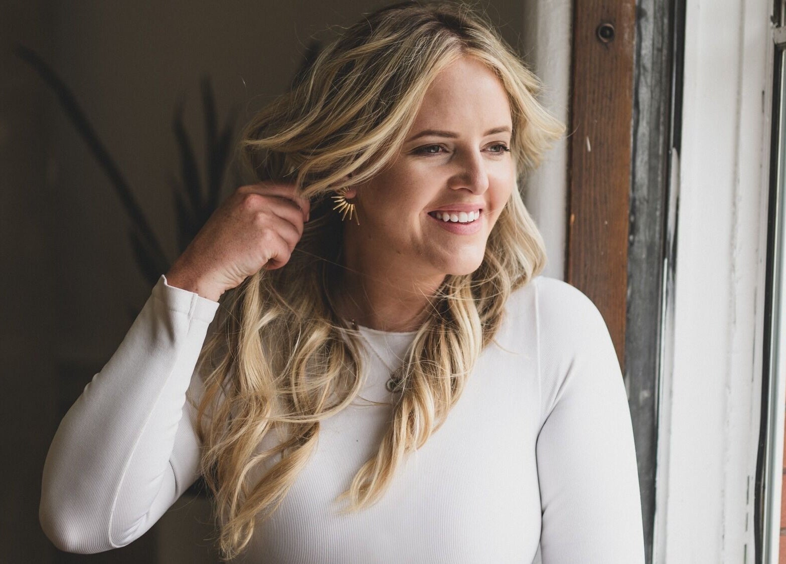 Smiling woman near window at Pura Vida Salon in Livingston, Montana. Stylish and welcoming interior.